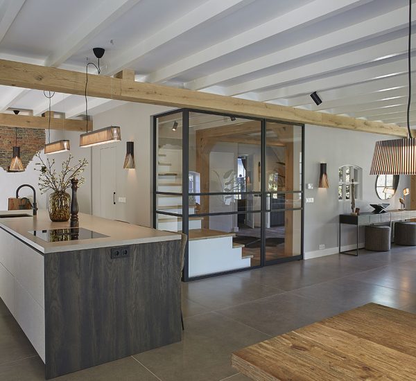 Keuken met centraal eiland, houten balken en glazen afscheiding naar hal.